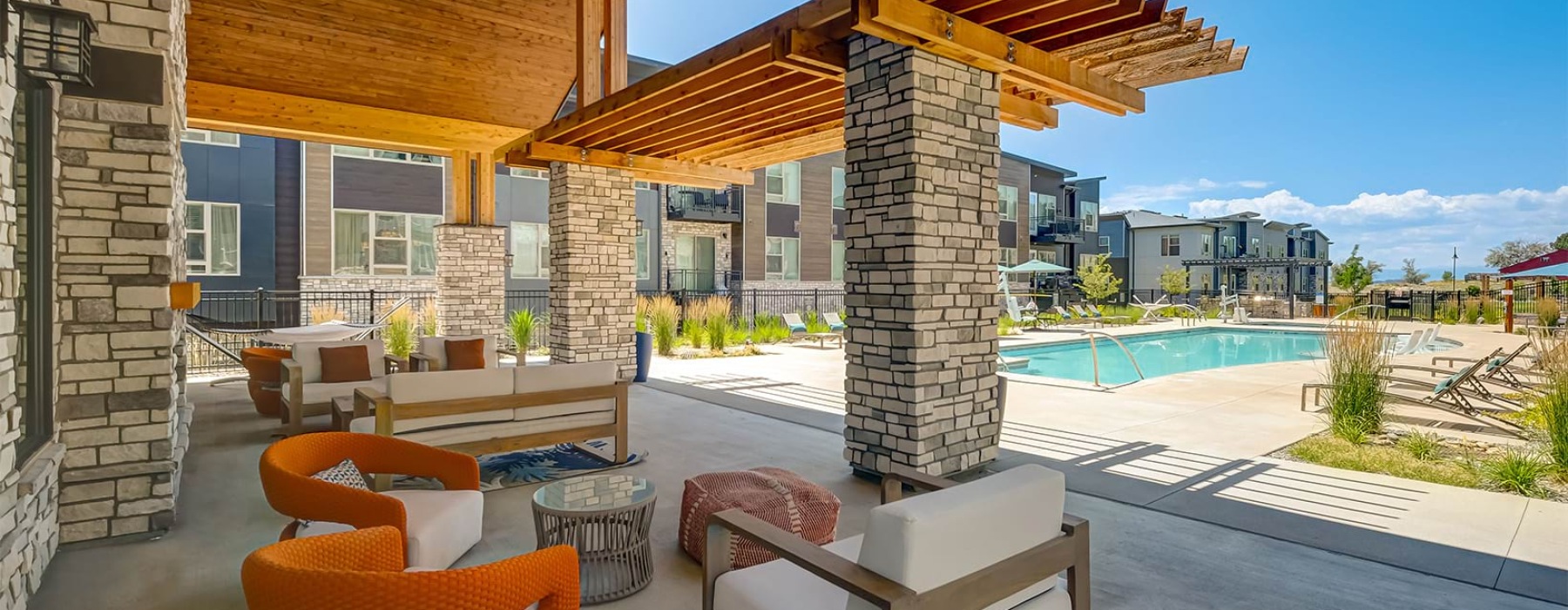 A shaded patio with chairs next to a pool at Broadstone Wren apartments in Parker, Colorado.